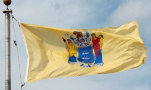 Yellow State Flag of New Jersey Waves in the Wind Against Cloudy Blue Sky