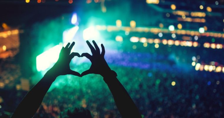 Fan Among Crowd of Fans Puts Up Hands Forming Heart While Watching Concert Displaying Bright Lights