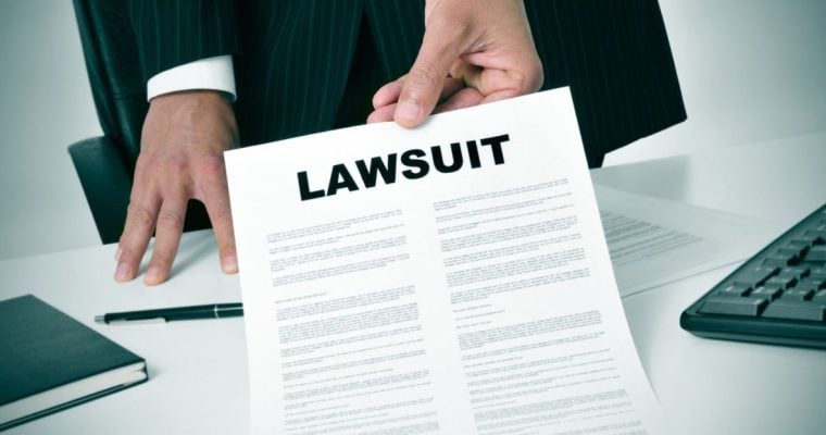 Man in Suit Holds Paper Reading Lawsuit Inside Office