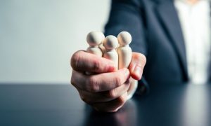 Human-Like Wooden Figures Squeezed in One Hand By Man in Business Suit