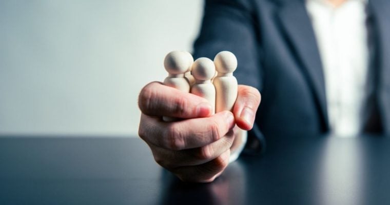 Human-Like Wooden Figures Squeezed in One Hand By Man in Business Suit