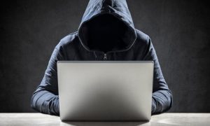 Faceless Man in Hood Sits At Laptop with Black Background