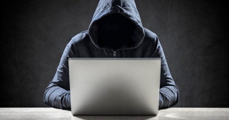 Faceless Man in Hood Sits At Laptop with Black Background