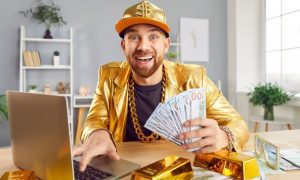 Man Using Laptop Wears Gold Hat and Suit and Holds Fan of $100 Bills