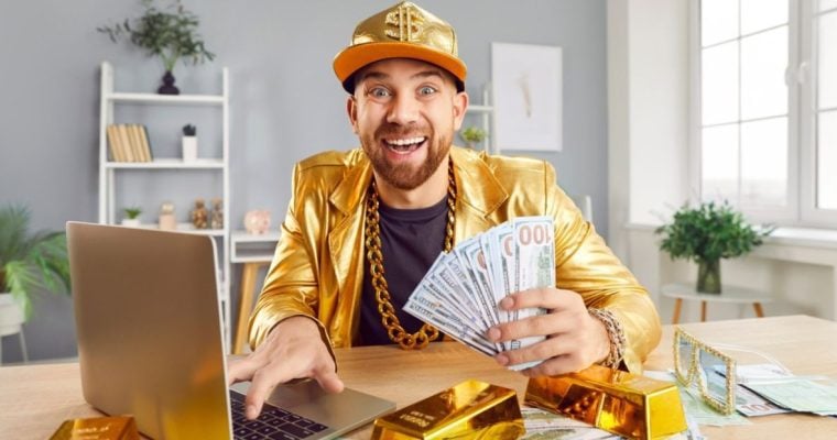 Man Using Laptop Wears Gold Hat and Suit and Holds Fan of $100 Bills