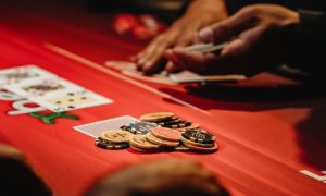 Hands Holding Cards At Red Poker Table With Stack of Chips