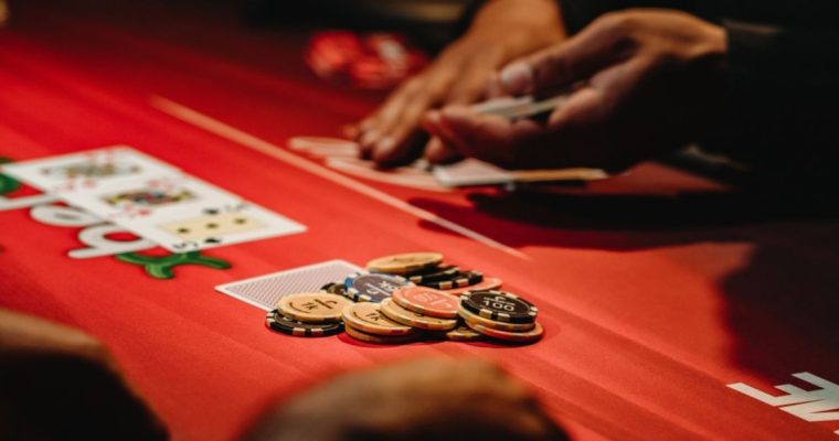 Hands Holding Cards At Red Poker Table With Stack of Chips