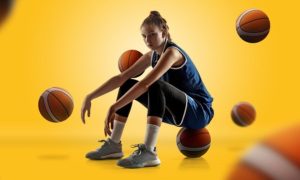 Female Basketball Player Sitting on Ball with Basketballs around on Yellow Background