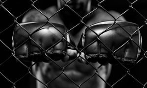 Man in MMA Fighting Cage Holds Fists with Black Gloves Up to Fence