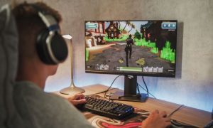 Young Man Plays PC Game on Desktop Computer and Wears Headphones