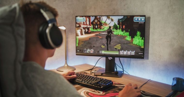 Young Man Plays PC Game on Desktop Computer and Wears Headphones