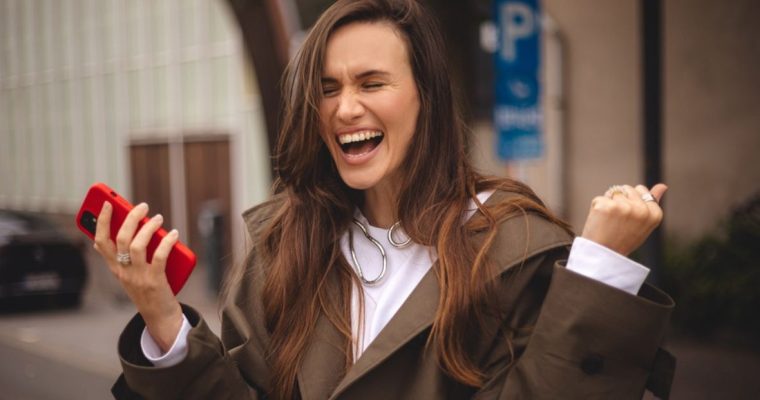 Woman With Excited and Happy Expression Holds Red Cell Phone