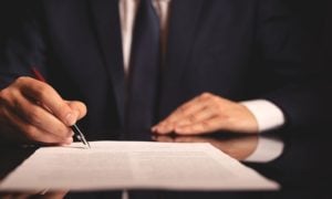 Man in Dark Suit Signs Document While Sitting at Desk