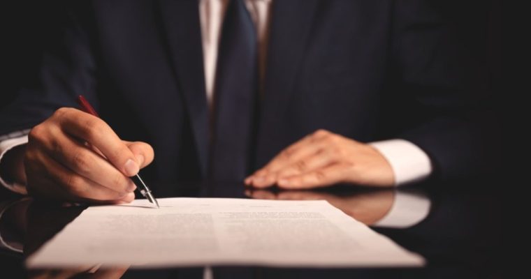 Man in Dark Suit Signs Document While Sitting at Desk