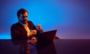 Man Sits At Desk in Front of Laptop With Excited Expression