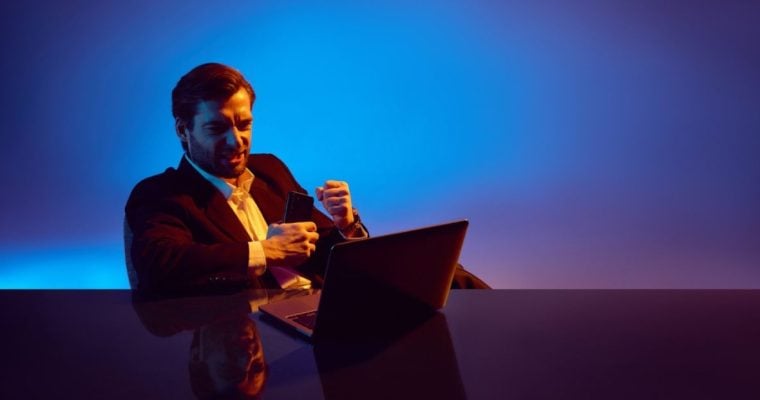 Man Sits At Desk in Front of Laptop With Excited Expression