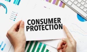 Desk With White Keyboard and Papers with Graphs Show Hands Holding Card Reading Consumer Protection