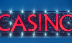 Huge Electric Red Sign Reads Casino with Bright White Spotlights Against Evening Blue Sky