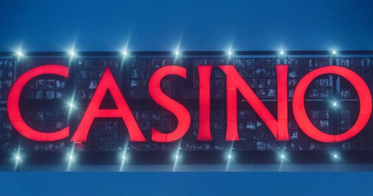 Huge Electric Red Sign Reads Casino with Bright White Spotlights Against Evening Blue Sky