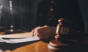 Man in a Suit Holding Pen Reviews Legal Documents Sitting at a Desk with Judge's Gavel