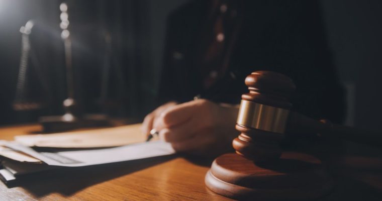 Man in a Suit Holding Pen Reviews Legal Documents Sitting at a Desk with Judge's Gavel
