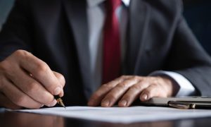 Businessman Holds Pen Ready to Sign Document Sitting at a Desk