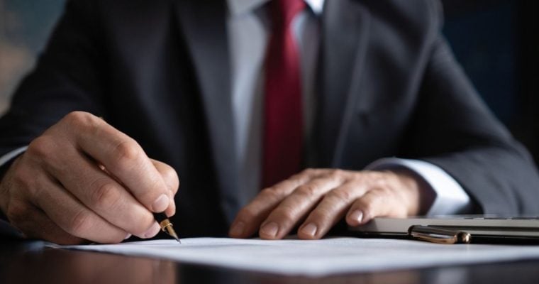 Businessman Holds Pen Ready to Sign Document Sitting at a Desk