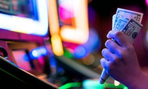 Woman's Hand Gribs Cash While Playing Brightly-Lit Slot Machine