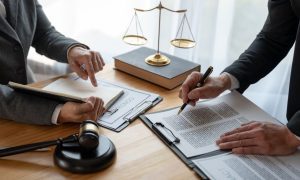 Two People in Suits Review Legal Documents on Desk with Gold Scale and Judge's Gavel