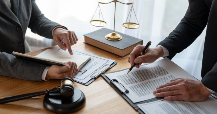 Two People in Suits Review Legal Documents on Desk with Gold Scale and Judge's Gavel