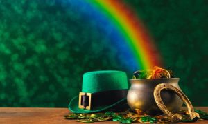 Rainbow Falls on Pot of Gold Coins Sitting Beside Leprechaun's Hat and Horseshoe