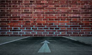 Red Brick Wall Blocks A Road with White Arrow Pointing To it