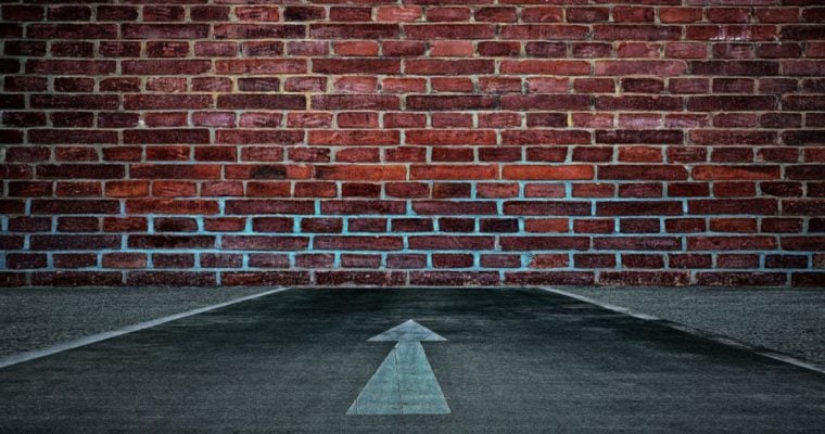 Red Brick Wall Blocks A Road with White Arrow Pointing To it