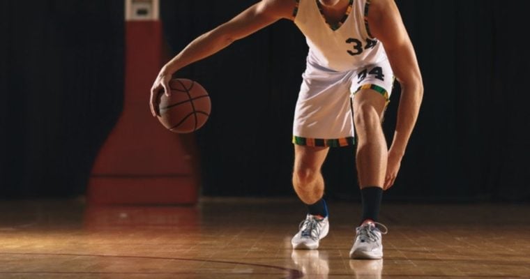 Young Man Bounces a Basketball On Empty Court