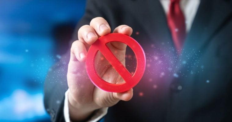Man Wearing a Suit with Red Tie Holds a Red Banned Logo