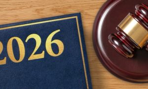 Wood Desk Displays Judge's Gavel Sitting Next to Blue Legal Book with 2026 in Gold Font