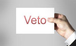 Man in Suit Holds White Paper with Red Veto Spelled on It