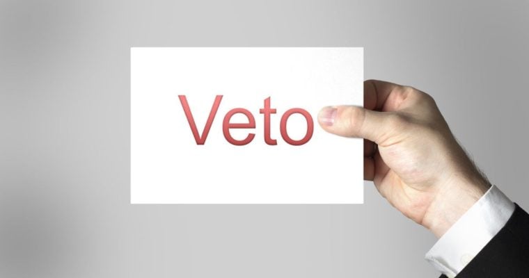Man in Suit Holds White Paper with Red Veto Spelled on It