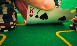 Green Poker Table with Hand Bending K and 7 Playing Cards Next to Stacks of Poker Chips
