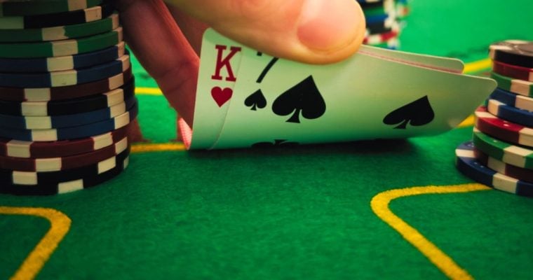 Green Poker Table with Hand Bending K and 7 Playing Cards Next to Stacks of Poker Chips