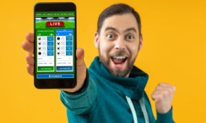 Excited Sports Fan Shows Cell Phone with Live Sports Betting Application on Yellow Background