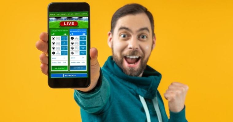 Excited Sports Fan Shows Cell Phone with Live Sports Betting Application on Yellow Background