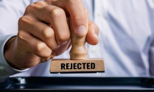 Man in Blue Shirt Holds Stamp with Text Reading Rejected in Black Font