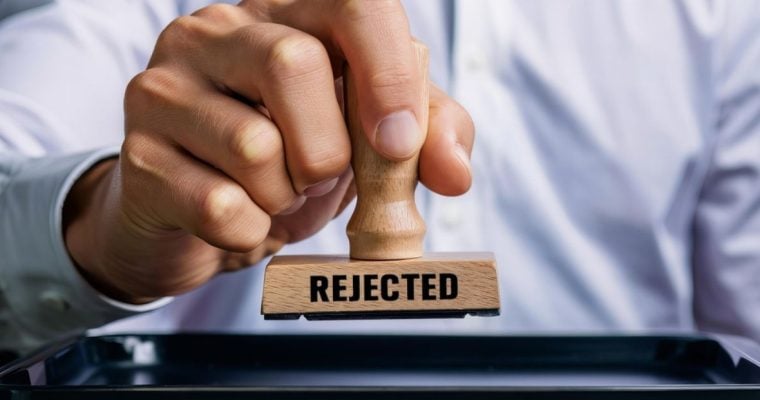 Man in Blue Shirt Holds Stamp with Text Reading Rejected in Black Font