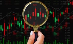 Red and Green Candlestick Graph with Hand Holding Gold Magnifying Glass Up to It