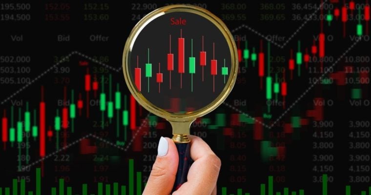 Red and Green Candlestick Graph with Hand Holding Gold Magnifying Glass Up to It
