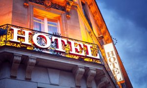 White Hotel Sign Sits on Metal Railing Outside Building with Yellow Light Shining Behind
