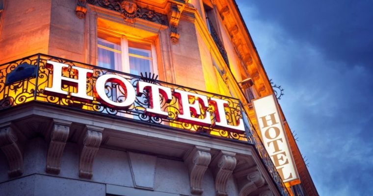 White Hotel Sign Sits on Metal Railing Outside Building with Yellow Light Shining Behind