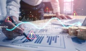 Man Analysis Documents with Bar Graphs In Front of Laptop with Digital Image Overlay of Wave Graph and Warning Icons