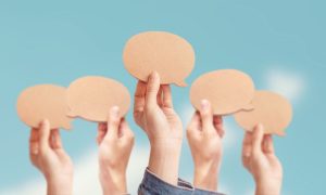 Hands Hold Up Blank Speech Bubbles Against Blue Sky Background